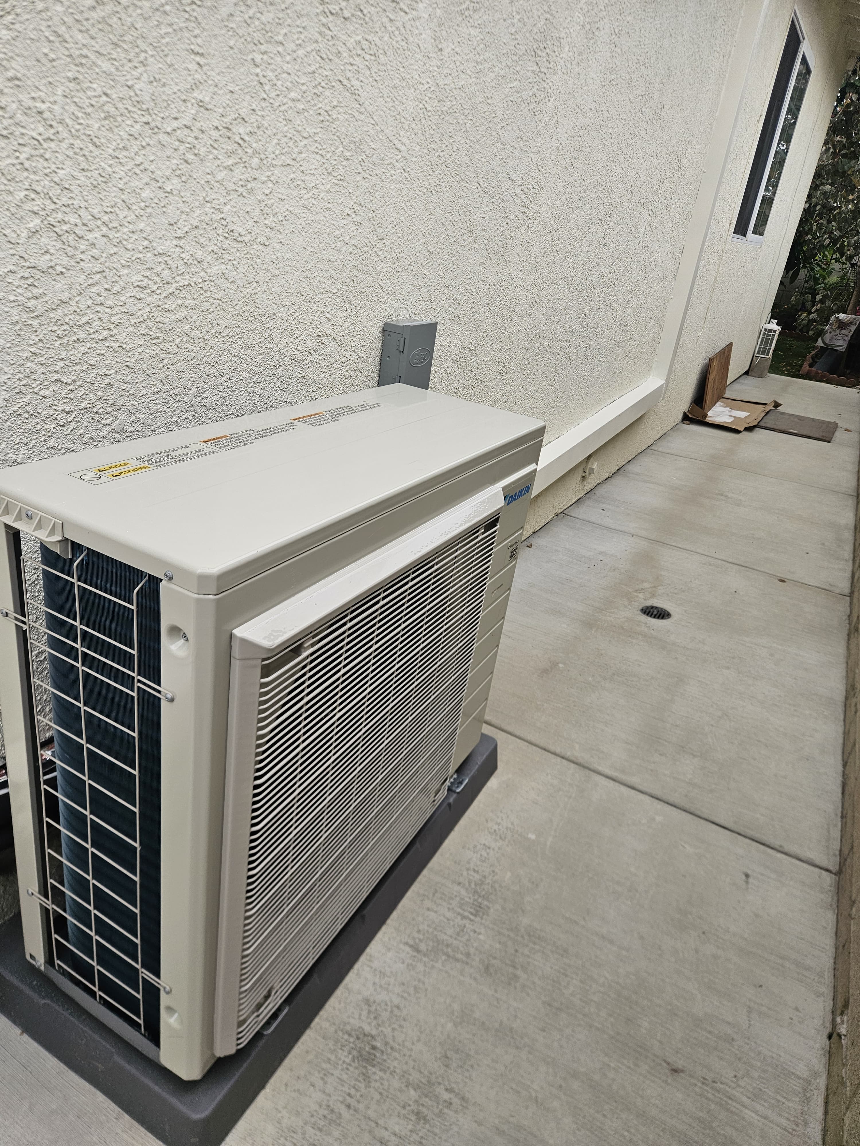 Cream-colored outdoor condensing unit installed on a concrete walkway beside a stucco wall