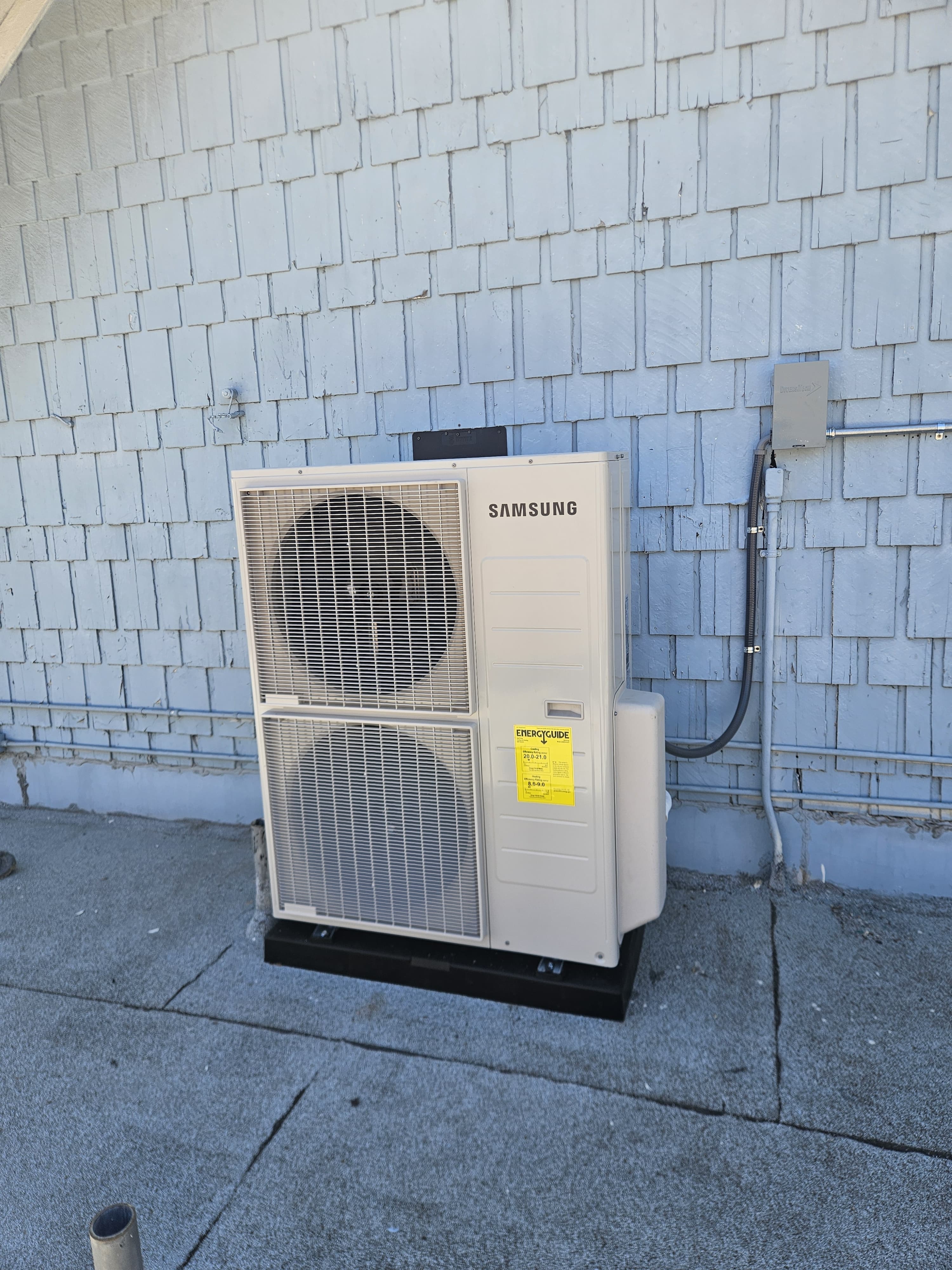 Samsung outdoor unit with two fans installed on a pad against a painted brick wall
