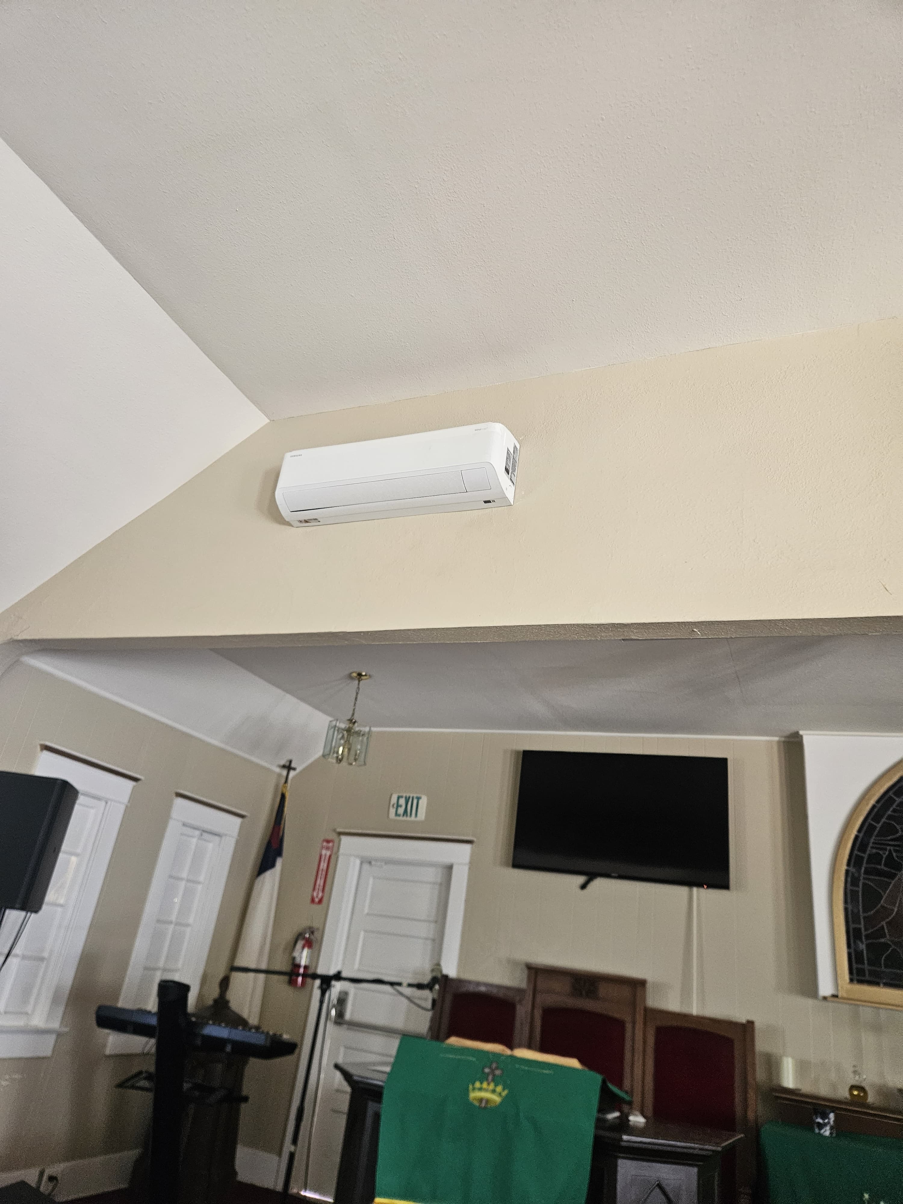 Wall-mounted mini-split head installed high on the wall of a meeting hall