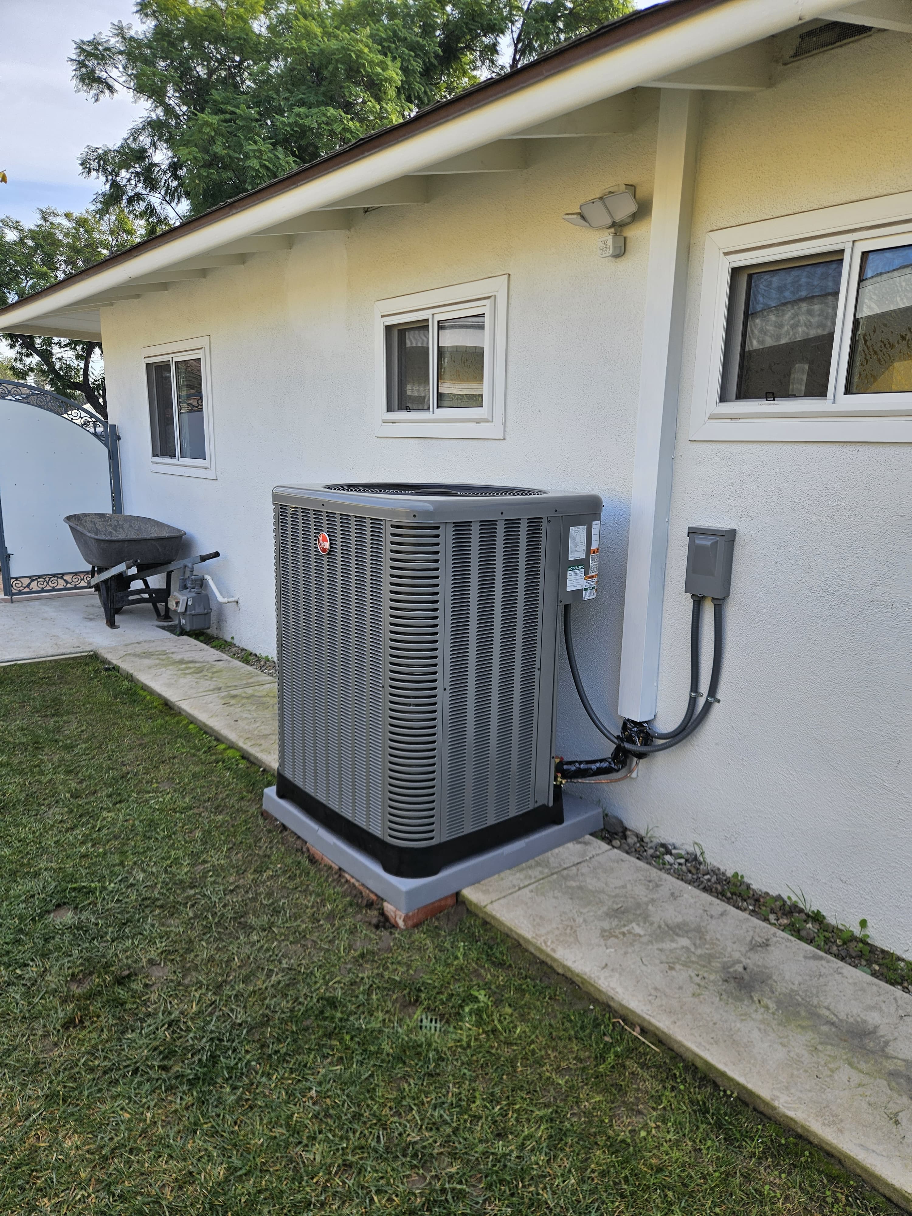 Rheem residential AC condenser installed on a pad beside a single-story home