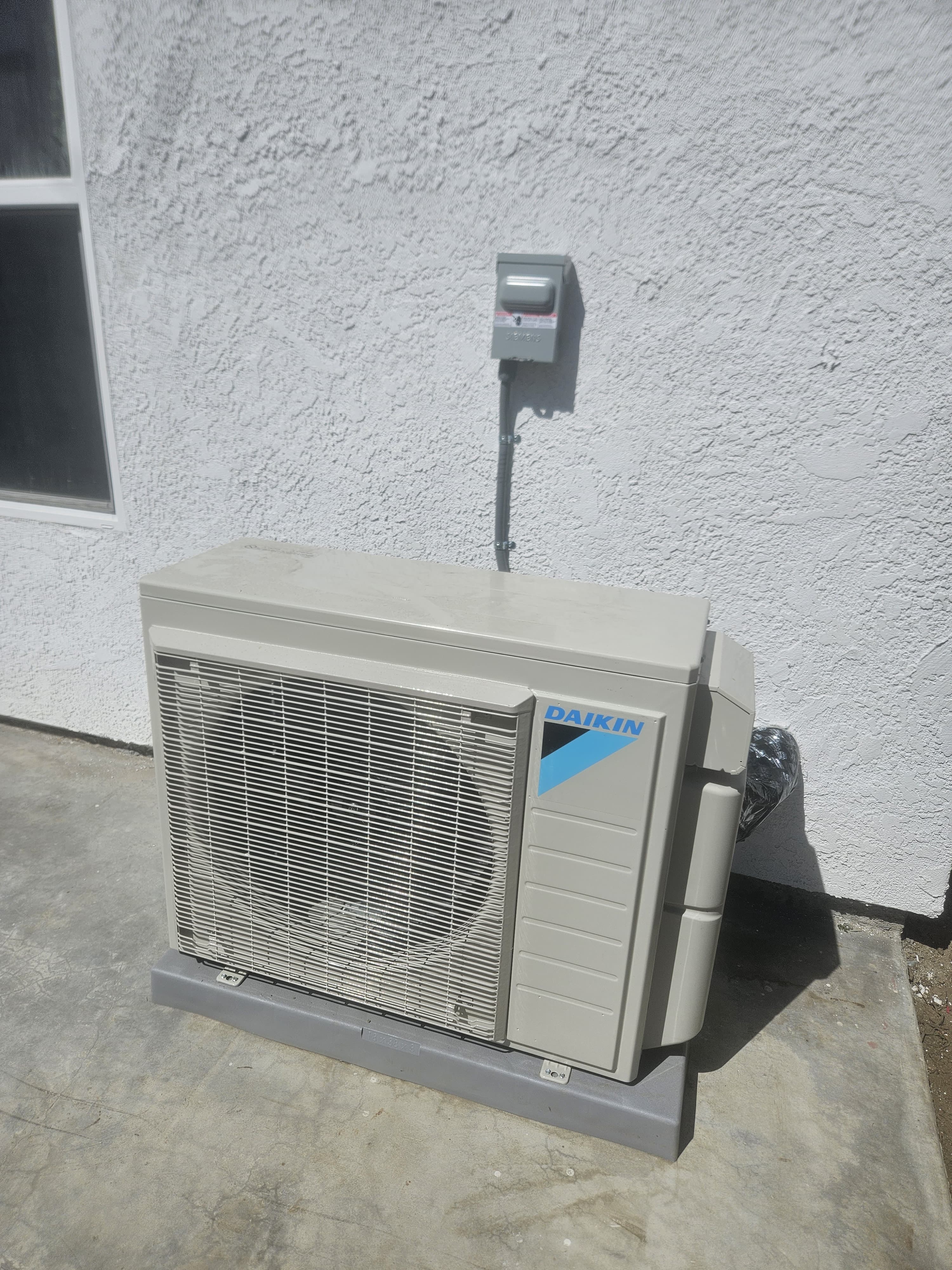 Unidad exterior Daikin sobre base de concreto con el disconnect eléctrico en la pared