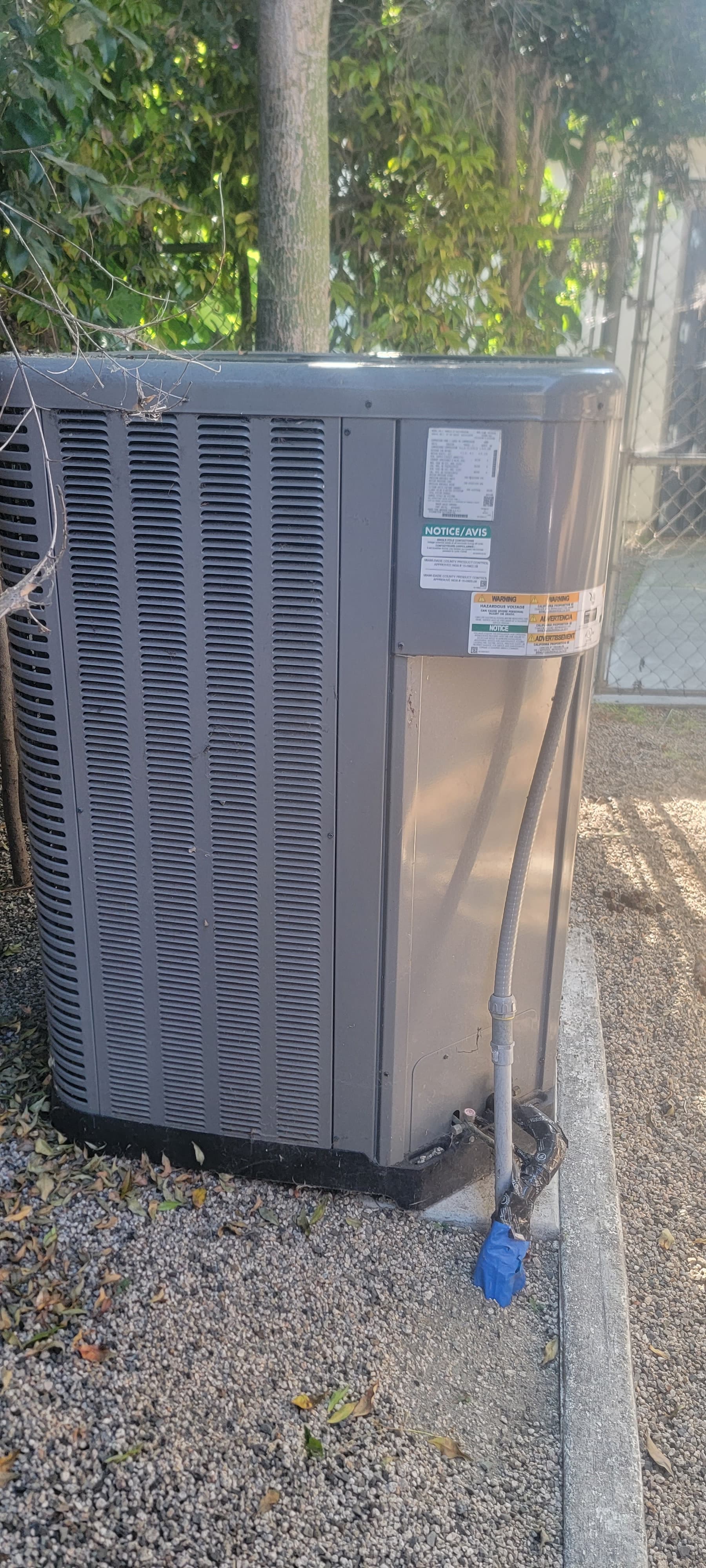 Condensador de AC exterior instalado sobre grava junto a una línea de árboles
